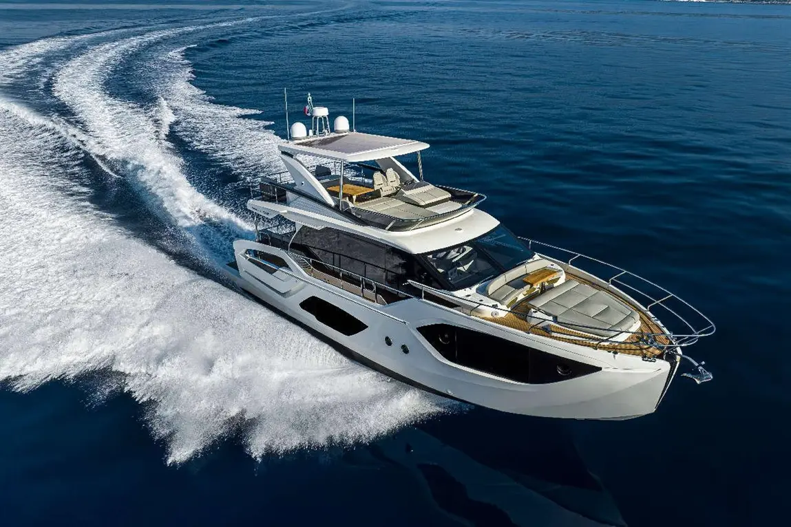 Luxury yacht cruising on calm waters, leaving a trail of white foam, showcasing sleek design and spacious sunbathing areas.